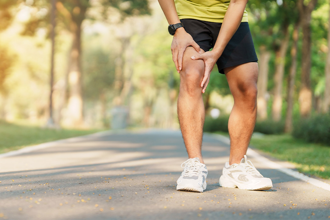 A man on a road, visibly in pain from his knee, highlighting concerns for runners during summer activities.
