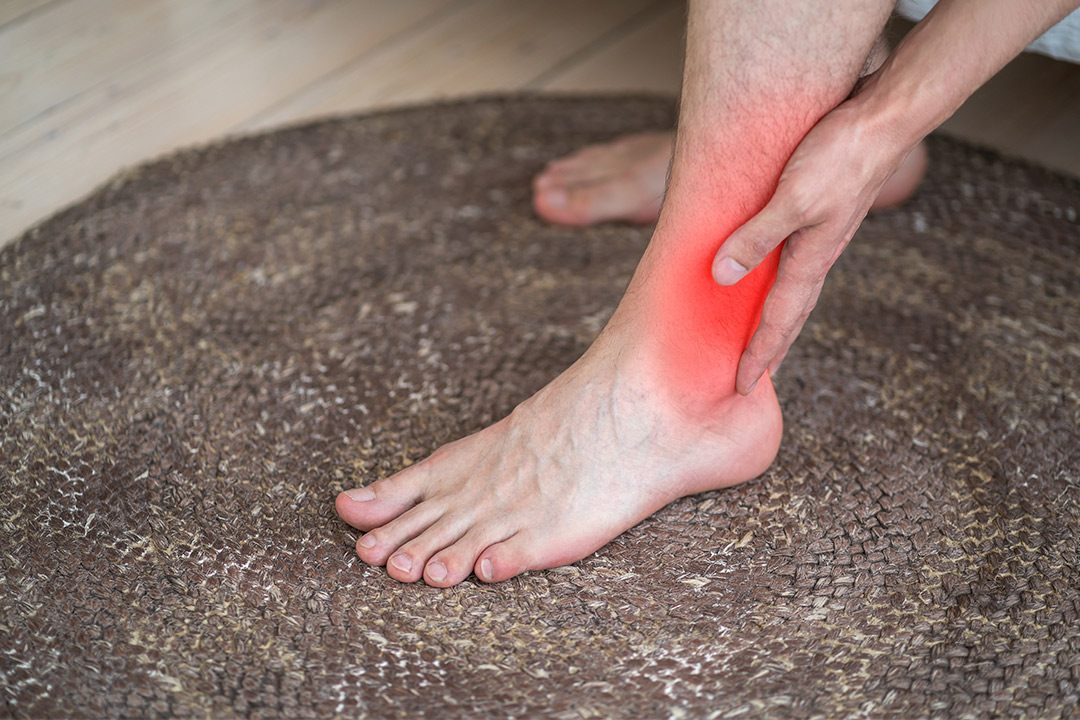 A person sits on a rug, visibly in pain, clutching their foot, emphasizing the need for tendon repair solutions.