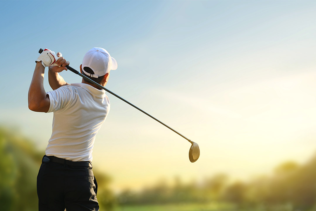A man swings his golf club at a ball, demonstrating a powerful golf stroke.