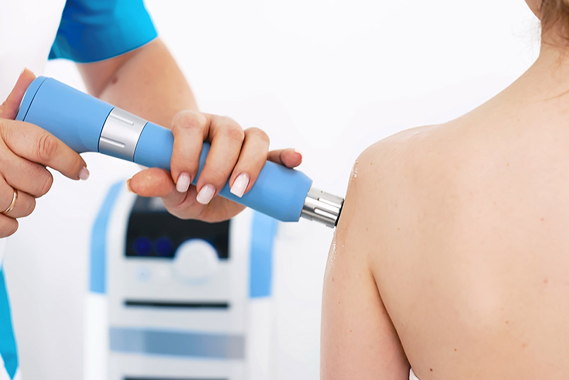 A woman applies shockwave treatment to her back, illustrating the benefits of PRP and shockwave therapy together.