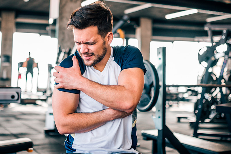In a gym, a man supports his arm, highlighting new studies on Shockwave and PRP for faster shoulder and elbow recovery.