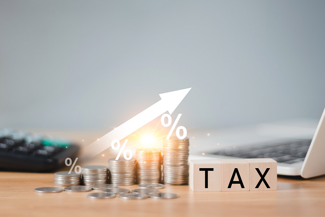 A tax calculator, coins, laptop, and calculator on a wooden table, illustrating end-of-year budgeting for machine costs.