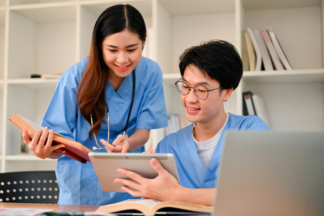 Asian nurse and student engaged in a laptop session, exploring online options for winter ESWT certification training.