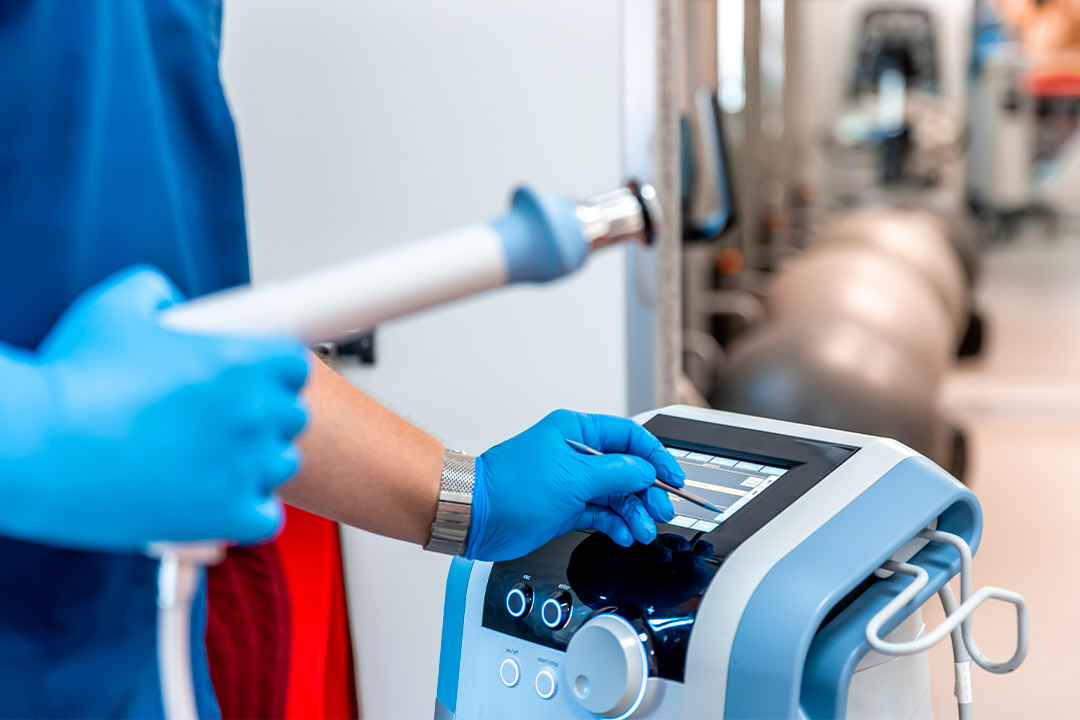 A person wearing blue gloves operates a shockwave machine, illustrating hands-on training for ESWT certification programs.