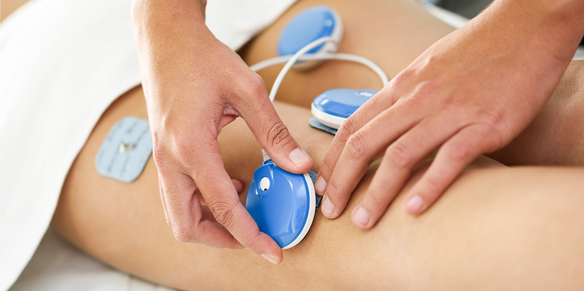  Individual applying an electric device to the skin, illustrating the use of shockwave therapy in a clinic.