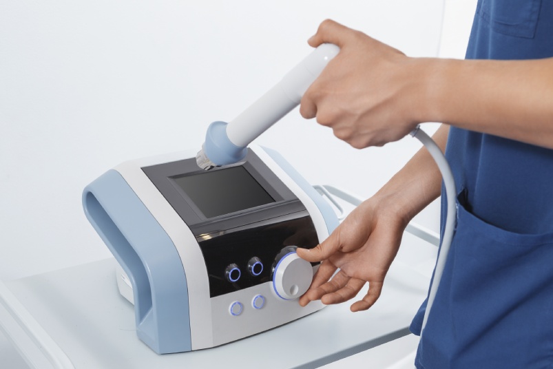 Physiotherapist adjusting shockwave therapy device. Close-up of hands operating medical rehabilitation equipment for pain relief and muscle recovery.