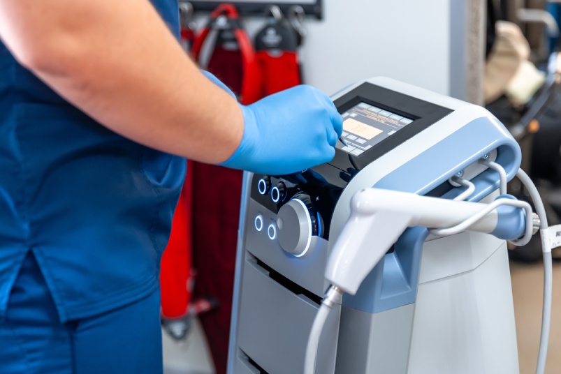 Shock wave therapy device with male doctor hands in rubber gloves.